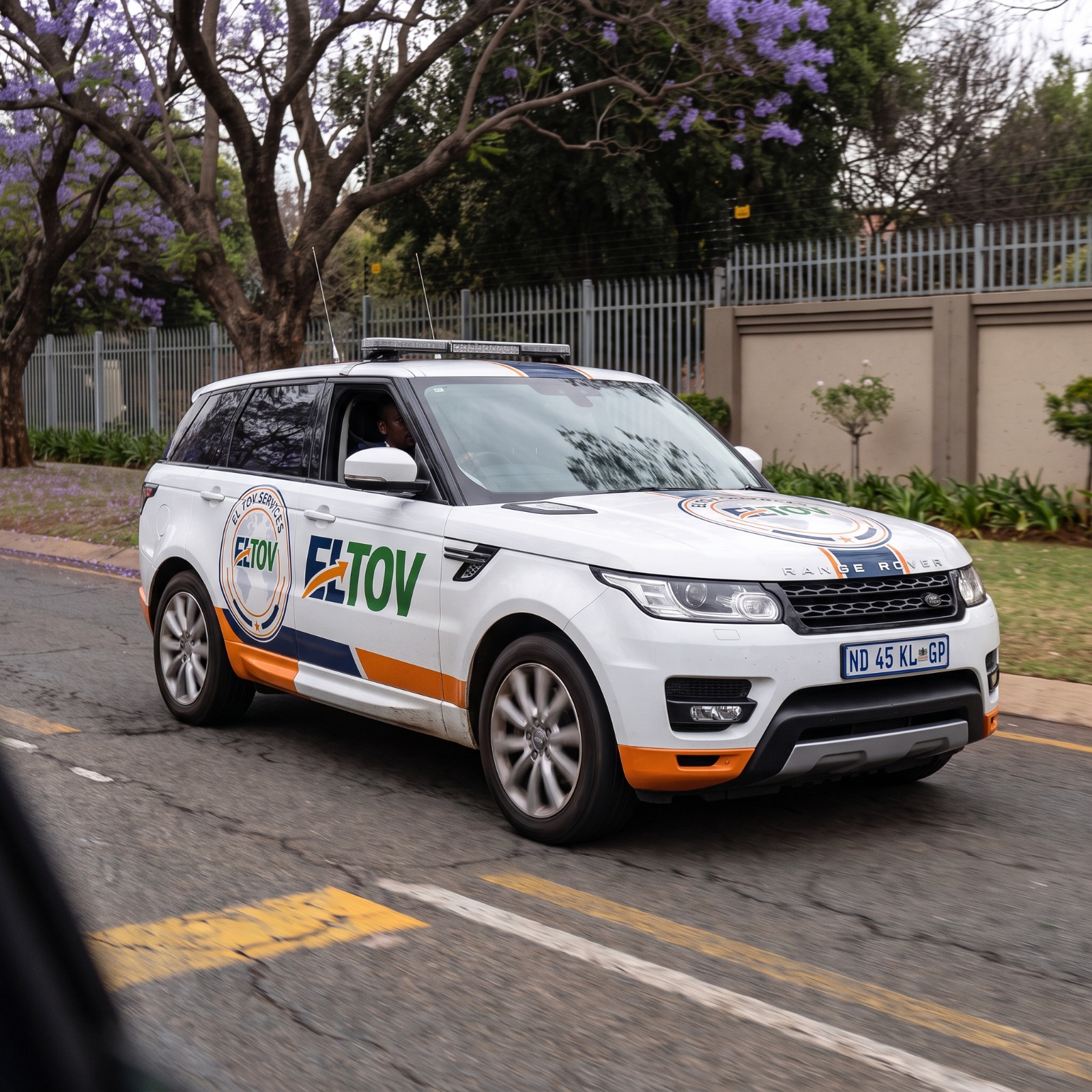 Eltov Security marked patrol vehicle on a jacaranda-lined suburban street